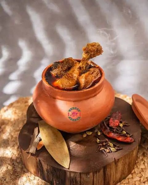 Chicken handi served in a traditional clay pot with whole spices on a wooden board